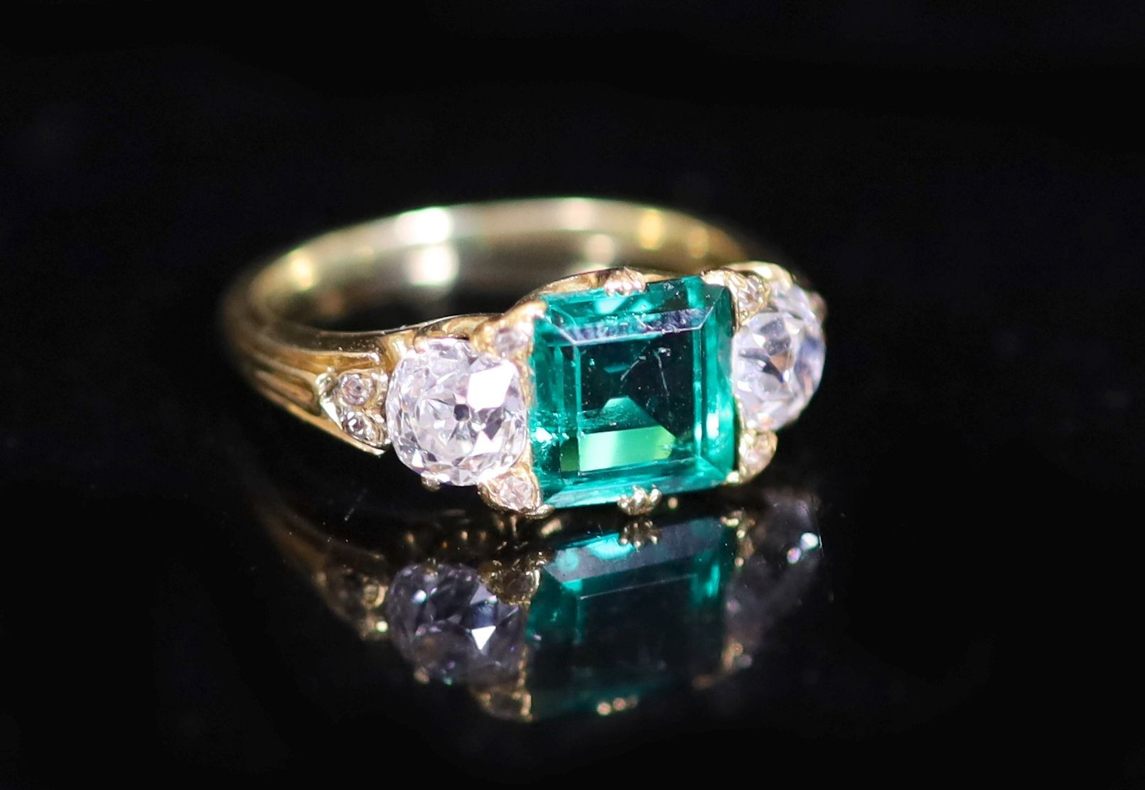 A good early 20th century gold, single stone trap cut emerald and two stone old cut diamond set ring